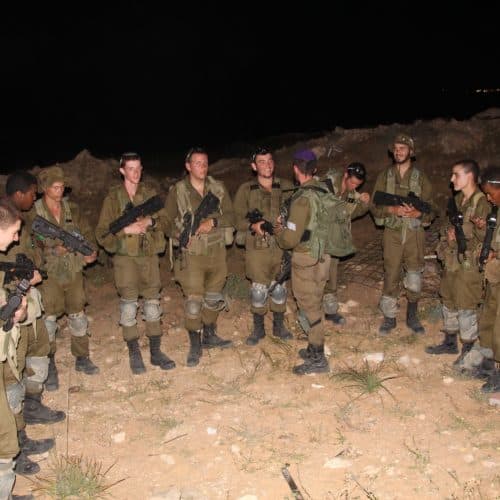 Un groupe de soldats armés, debout en demi-cercle en terrain découvert, de nuit