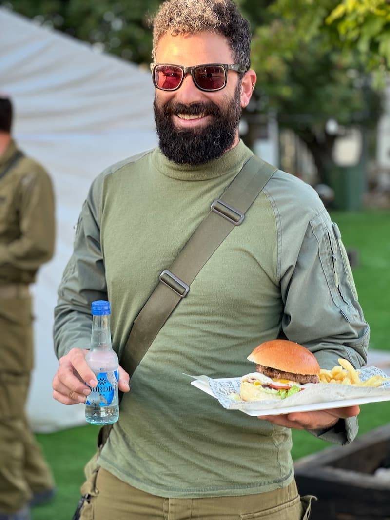 גבר מזוקן עם משקפי שמש מחייך ומחזיק מגש עם המבורגר וצ׳יפס ובקבוק שתייה