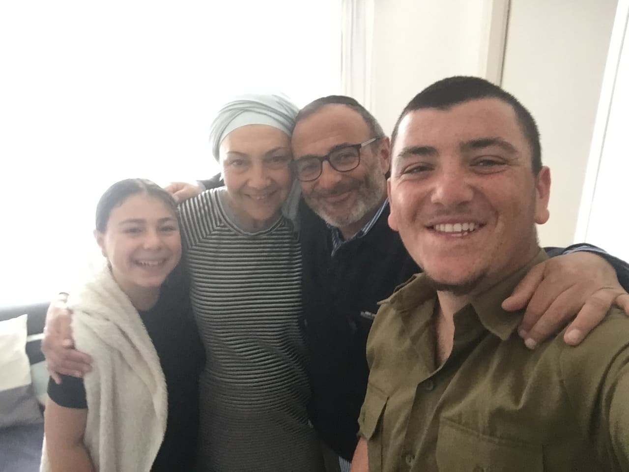 Elkana en uniforme se prend en selfie, souriant, aux côtés d’une jeune fille, d’une femme et d’un homme enlacés