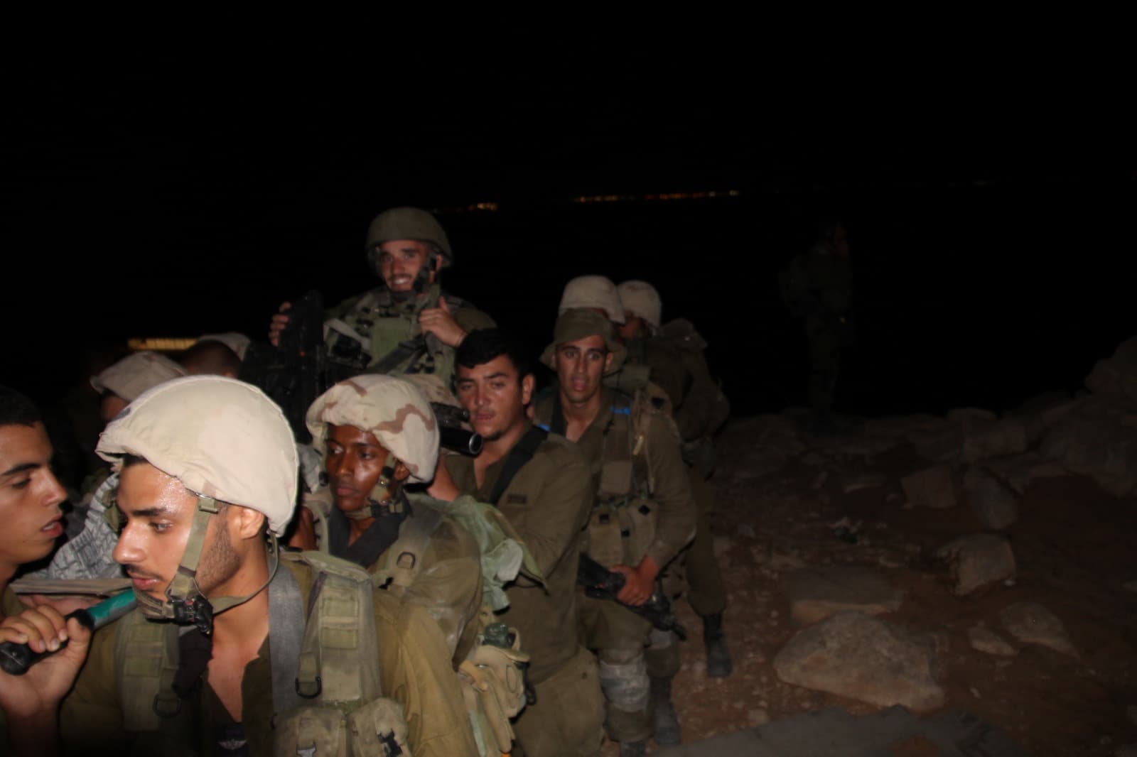 Des soldats casqués, assis serrés les uns contre les autres, de nuit