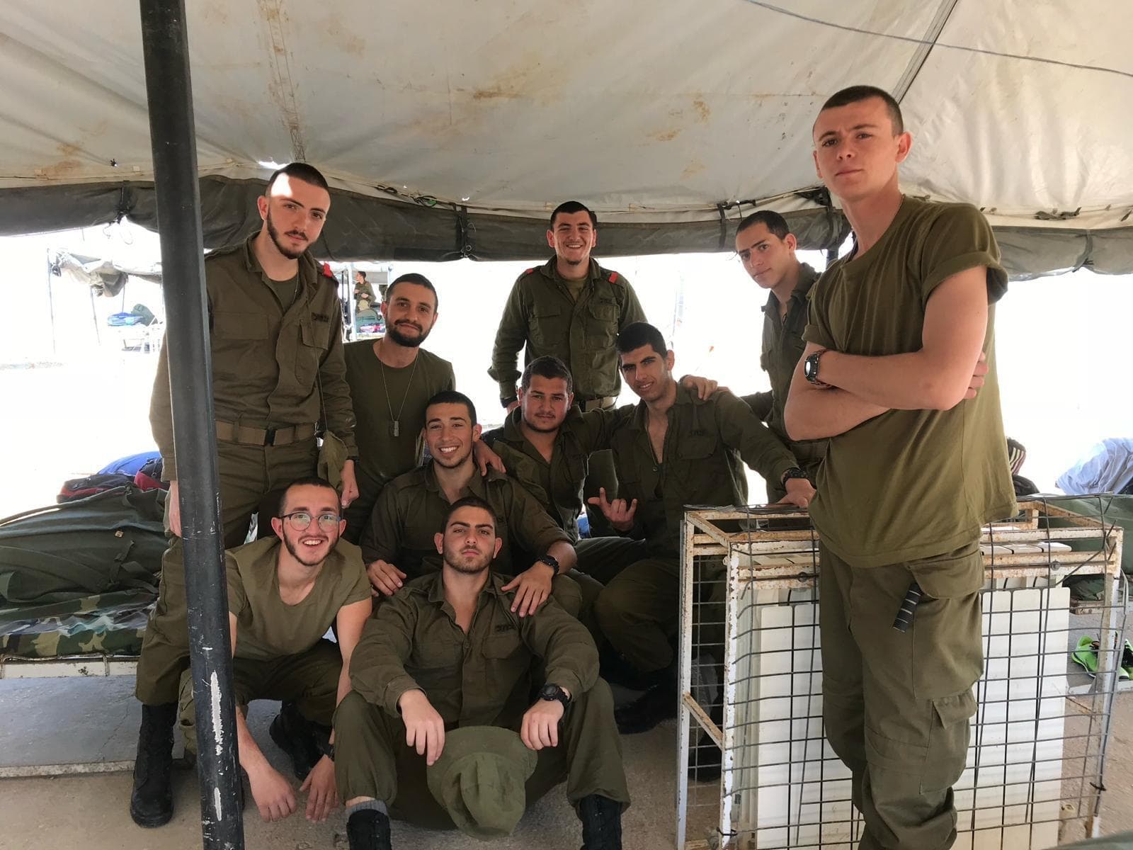 Un groupe de soldats sourit sous un abri, certains assis, d’autres debout