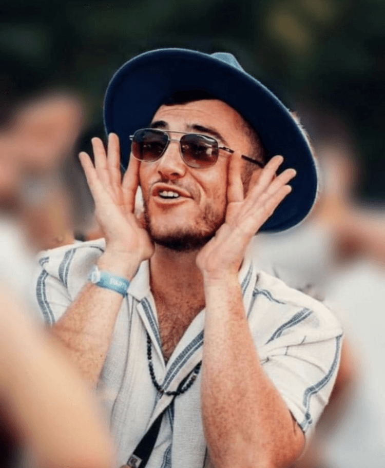 Elkana, chapeau et lunettes de soleil, les mains en porte-voix, crie de joie